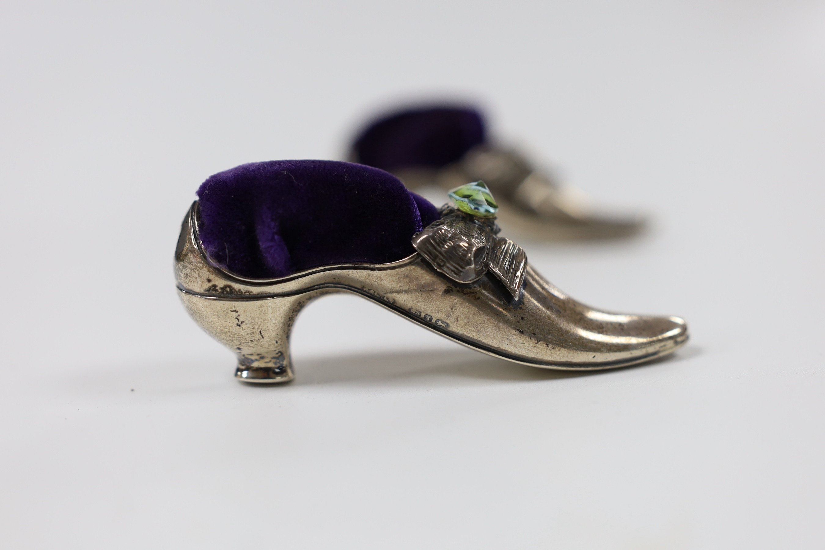 Two similar late Victorian novelty silver mounted pin cushions, modelled as shoes, one set with later green stone, Adie & Lovekin, Birmingham, 1890, length 83mm (later cushions).